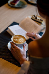 A Cup of coffee and an open book in a woman's hand