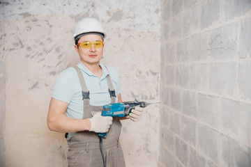 Portrait man builder repairer in protective glasses, hard hat, overalls showing having equipment in arm on grey background home brick