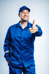 Portrait of young worker man wearing blue uniform. Pointing finger at you looking at camera. Isolated on grey background with copy space. Human face expression, emotion. Business concept.