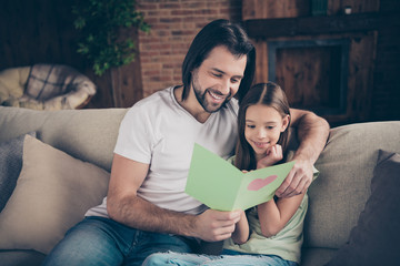 Photo of little pretty funny lady her handsome daddy sit cozy sofa hugging hold cute card birthday present reading greeting celebrate words best holiday house room indoors