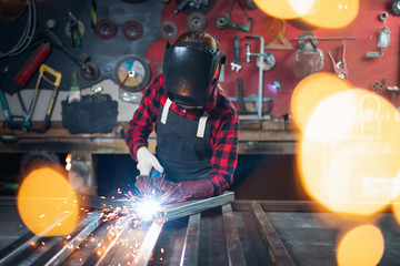 Worker welder on steel structure in factory, light spark