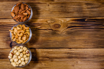 Various nuts (almond, cashew, hazelnut) in glass bowls on a wooden table. Vegetarian meal. Healthy eating concept. Top view