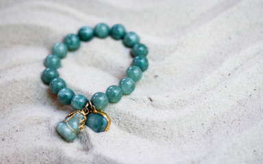 Natural semiprecious stone bracelet jewelry Beautiful synthetic stone beads on a sand background.