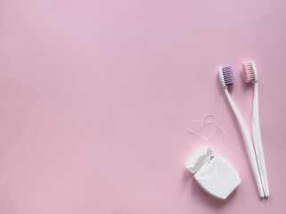 on a pink background, two toothbrushes with white handles and pink and purple bristles hug. next...