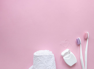 on a pink background, two toothbrushes with white handles and pink and purple bristles hug. next lies dental floss in the form of a heart and a white towel copy space
