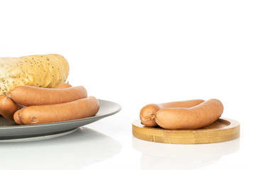 Group of five whole pork frankfurt sausage on gray ceramic plate on round bamboo coaster with  bread roll isolated on white background