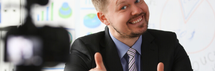 Male in suit and tie show confirm sign arm making promo videoblog or photo session in office camcorder to tripod portrait. Vlogger promotion selfie solution or finance advisor management information © H_Ko