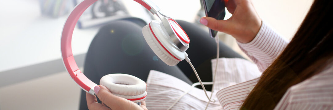 Young beautiful woman headphones holds smartphone in hand using at home costs about sofa. Verifies internal information its financial advertising freedom makes money level transfer contractor concept