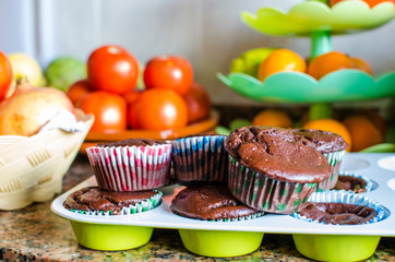 Photograph of homemade chocolate and vegan muffins with fruit and vegetables in the background in the home kitchen