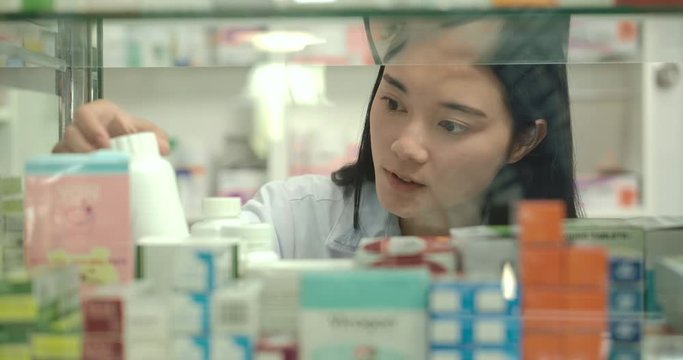 Young asian pharmacist woman looks at the medicines in the pharmacy window.