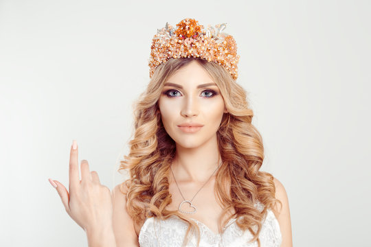 Woman with the crown shows come here gestures with her index finger right hand, white background. Woman wearing crown, bride princess miss picture for beauty magazines white light gray background wall