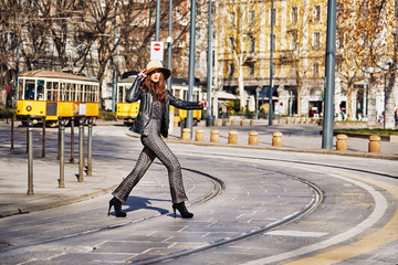 Model crossing the street with cable cars (Trams) at the background in Milan Italy during the day