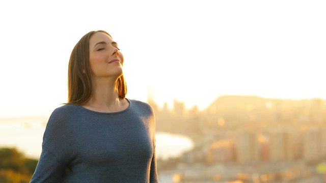 Woman relaxing breathing deeply fresh air in city outskirts at sunset