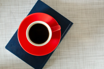 Red cup of coffee on dark blue notebook on white texture background. Flat lay. Copy space
