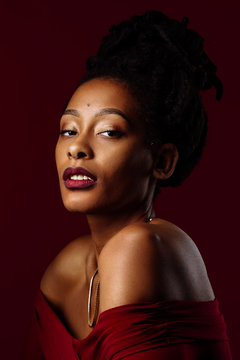 Studio portrait of a woman with dreadlocks wearing a red dress in a studio portrait with red background