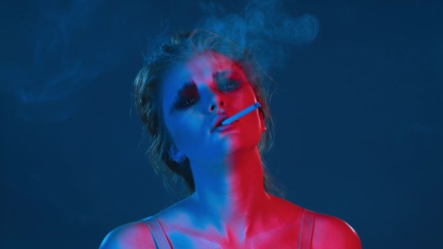 beautiful sexy lady Smoking cigarette at neon retro party drunk or high and looking at camera, young woman harming her health, nicotine addiction