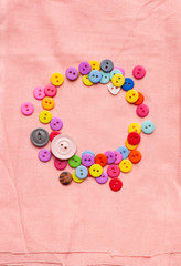 Bright multicolored buttons in the shape of a circle on a light pink fabric