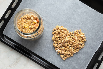 Granola in glass jar and heart on parchment paper on baking sheet, above. Made homemade granola, healthy breakfast concept