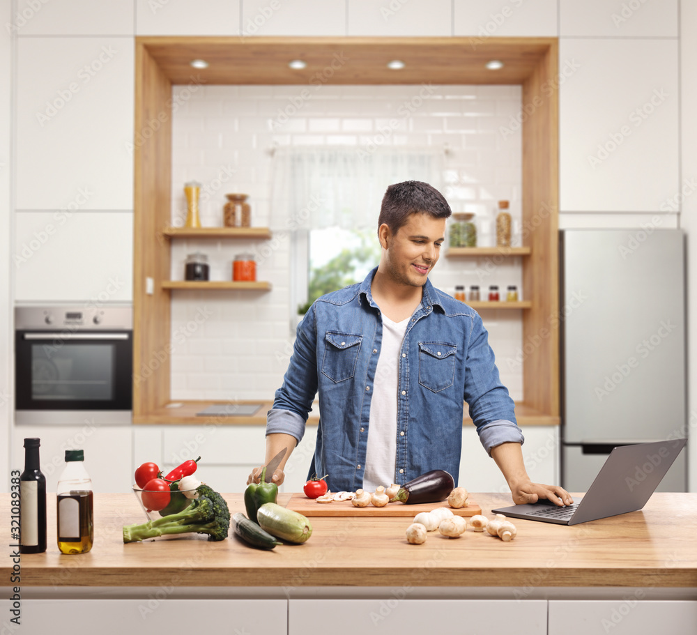 Wall mural young man cooking in a kitchen with a laptop