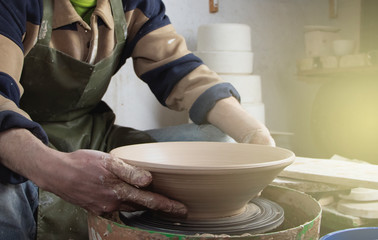 Hands of a potter on a pottery wheel close-up. Old traditional art, handmade, clay and ceramic production. Pottery workshop in subdued soft light