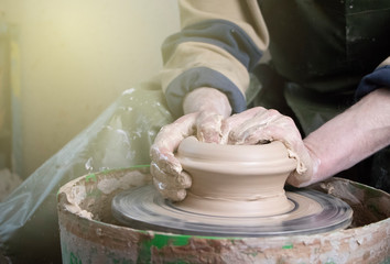 Hands of a potter on a pottery wheel close-up. Old traditional art, handmade, clay and ceramic production. Pottery workshop in subdued soft light