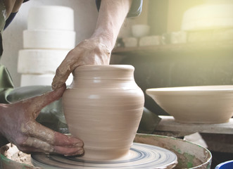 Hands of a potter on a pottery wheel close-up. Old traditional art, handmade, clay and ceramic production. Pottery workshop in subdued soft light