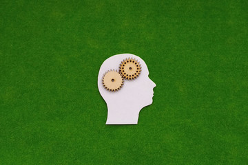 Silhouette of a human head, a pair of wooden gears on a green background.