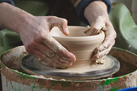 Hands of a potter on a pottery wheel close-up. Old traditional art, handmade, clay and ceramic production. Pottery workshop in subdued soft light