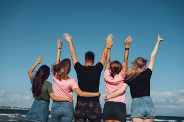Five friends raise their hands to sky with sea background
