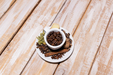 Cup with coffee beans and plate with spices for cooking coffee on wooden rustic background