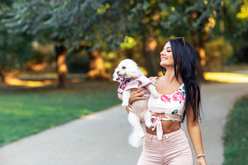Fashion girl in park in pink walk with her small dog on her hand