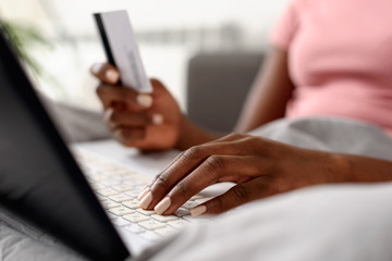 Young smiling African-American woman shopping over internet in the bed in the morning. E-banking and online shopping concept