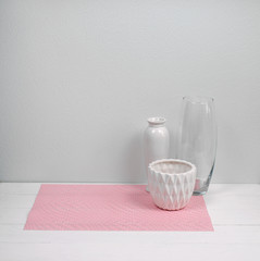 Interior decoration of a house, pot, glass and ceramic vase on pink napkin, white wood background. Modern interior. Minimalism style.