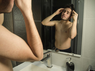 Portrait of handsome caucasian teenager reflection in from of the mirror, combing or brushing his hair