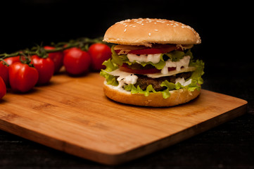 American burgers on a wooden Board with tomatoes on a dark background
