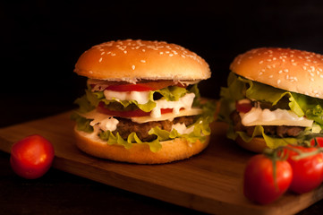 American burgers on a wooden Board with tomatoes on a dark background