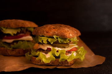 Russian burgers on tracing paper or food paper with tomatoes on a dark background