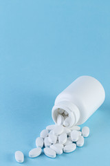 Pills spilling out of white bottle on blue background. with copy space. Pharmaceutical medicament, cure in container for health. Medicine concept