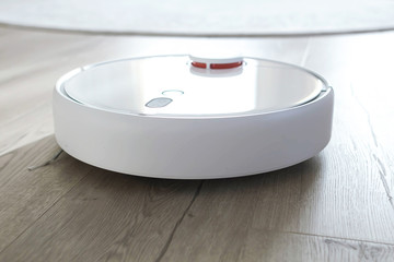 White robot vacuum cleaner on laminate floor. Modern smart device cleaning floor.