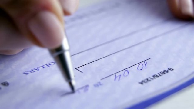 Young business woman filling a banking cheque check. Writing a cheque for payment