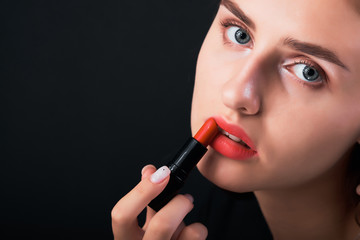 Obraz premium Close-up portrait of young girl painting her lips with red lipstick.