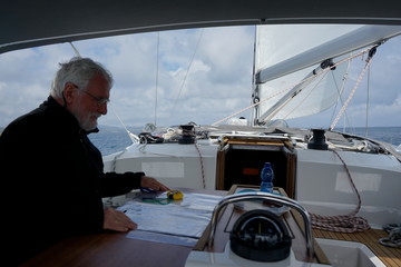 White bearded sailing senior, experienced skipper is reading a nautical chart  on a sailboat
