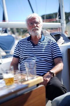 White bearded sailman senior, experienced skipper on a sailboat with evening beer after a sailing day