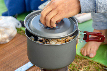 Camping food making. Pasta on pan on tourist fire stove. Camp cooking a mushroom soup at the lake shore.