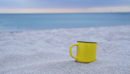 Yellow cup on sand background.