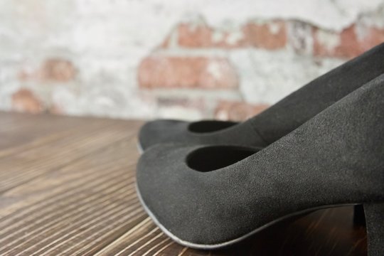 Black suede court shoes with brick wall in the background