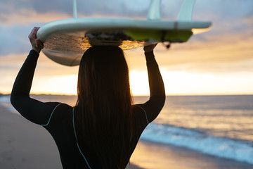 Back view of a young woman in the beach holding on her surfboard