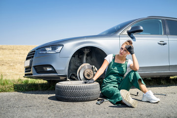 woman working with broken wheel of her car, waiting for help.