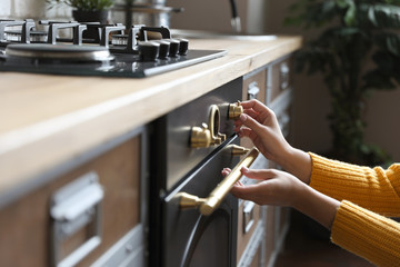 Woman using modern oven in kitchen, closeup