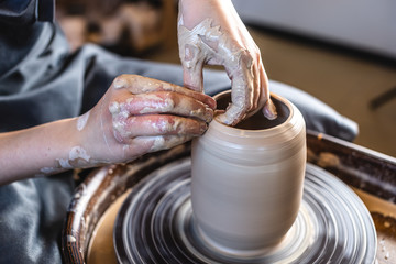 Potter working on a Potter's wheel making a vase. Woman forming the clay with her hands creating jug in a workshop